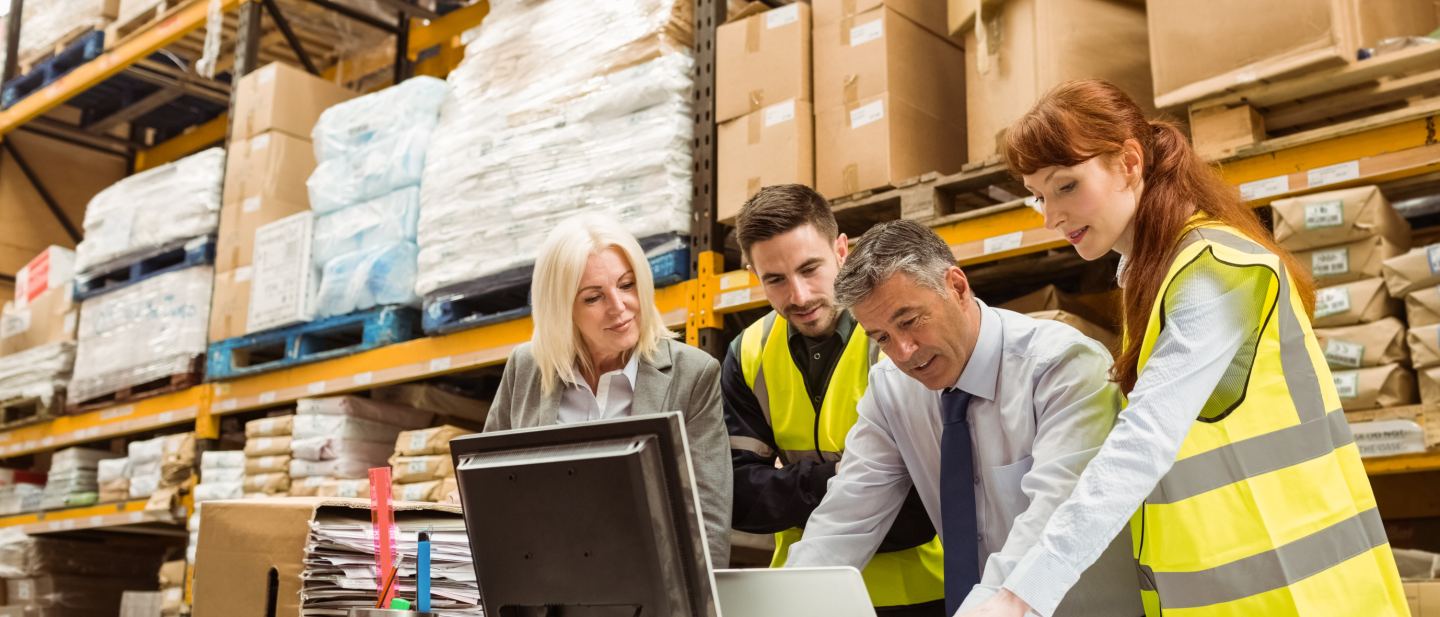 Warehouse managers and a worker reviewing inventory information in a large industrial facility